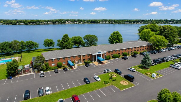 A hotel with a swimming pool, parking lot, and a view of a lake.