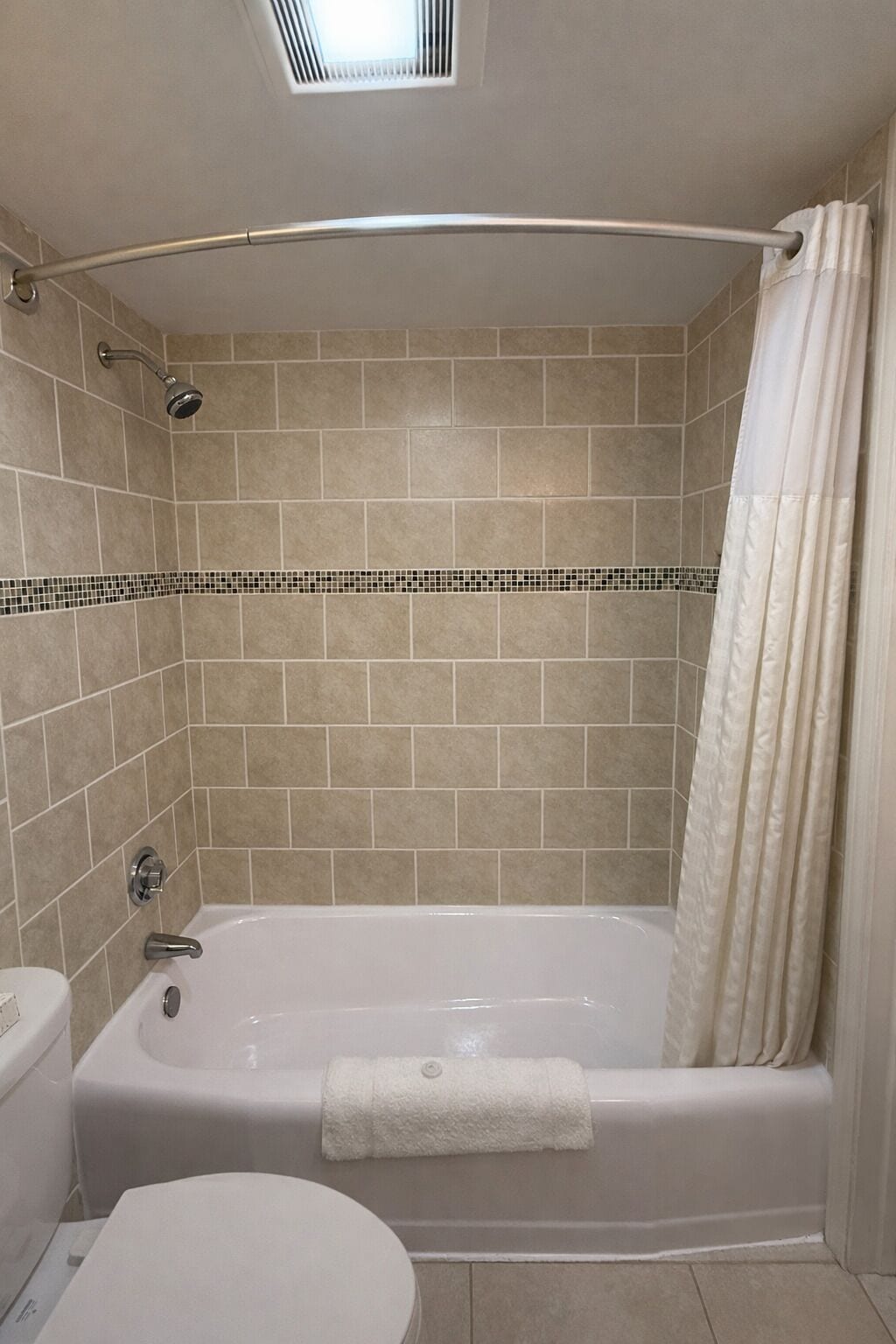 Et badeværelse med badekar, toilet og bruseforhæng.