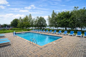 A rectangular swimming pool with blue water, surrounded by a brick deck. There are blue lounge chairs aligned on both sides of the pool. - Lakeside Inn (Wakefield)