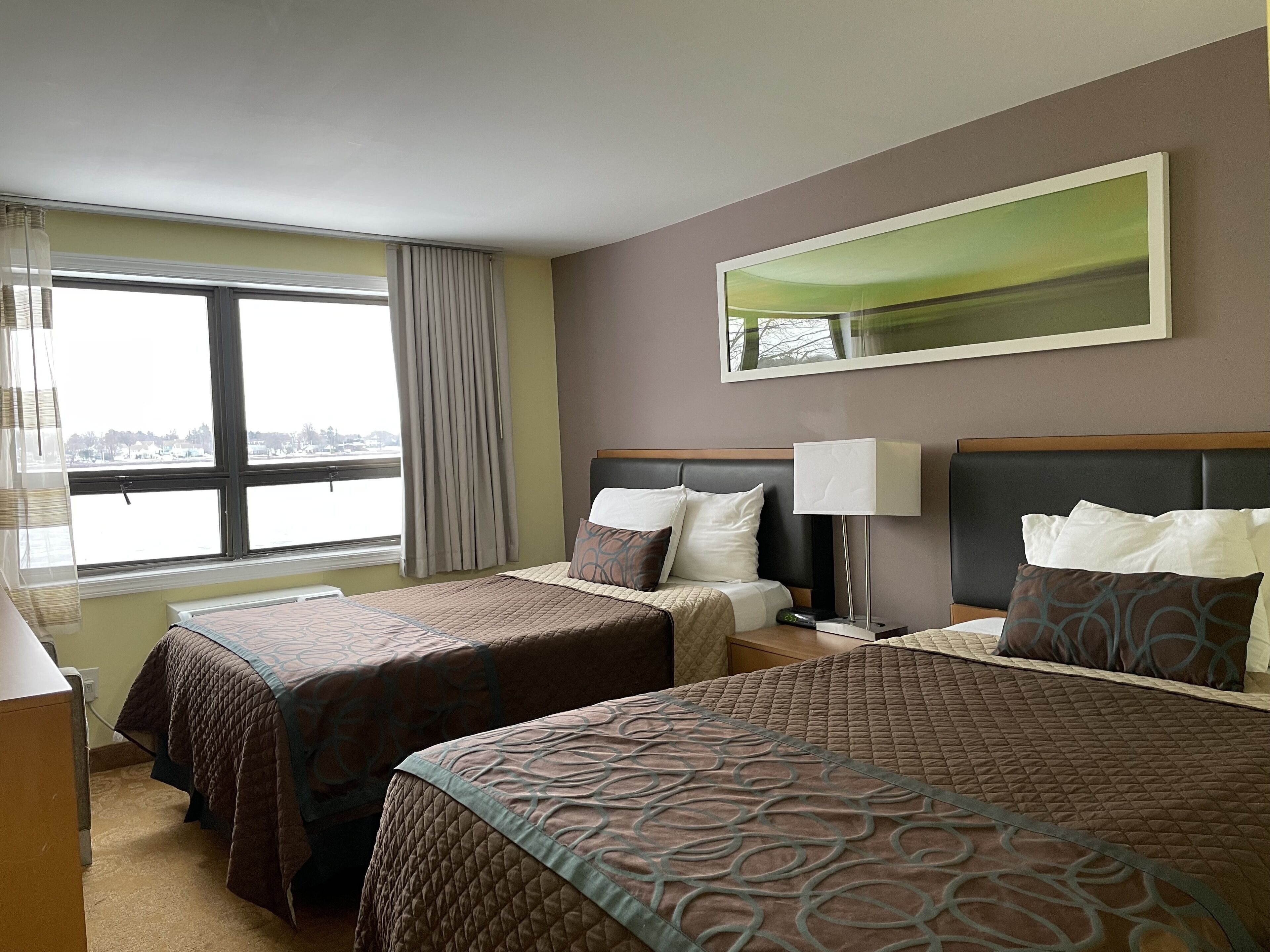 Ett hotellrum med två sängar, ett stort fönster, en spegel och en lampa.