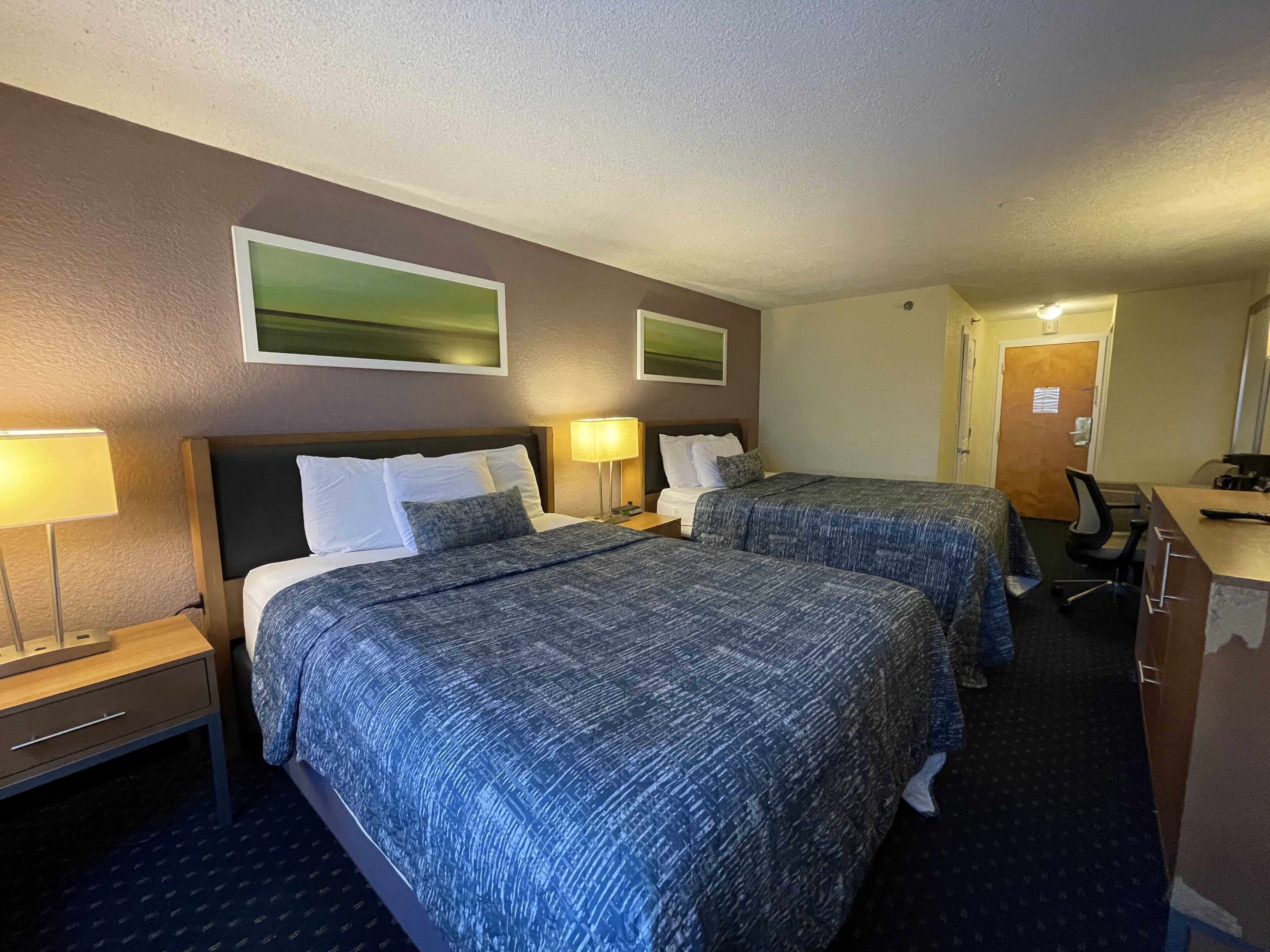 A hotel room with two beds, a desk, and a chair.