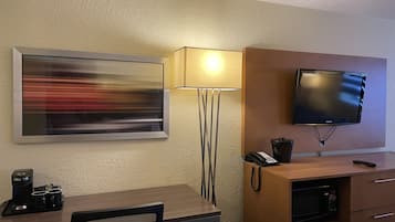 Habitación de hotel con escritorio, silla, cafetera, lámpara, televisor y microondas.