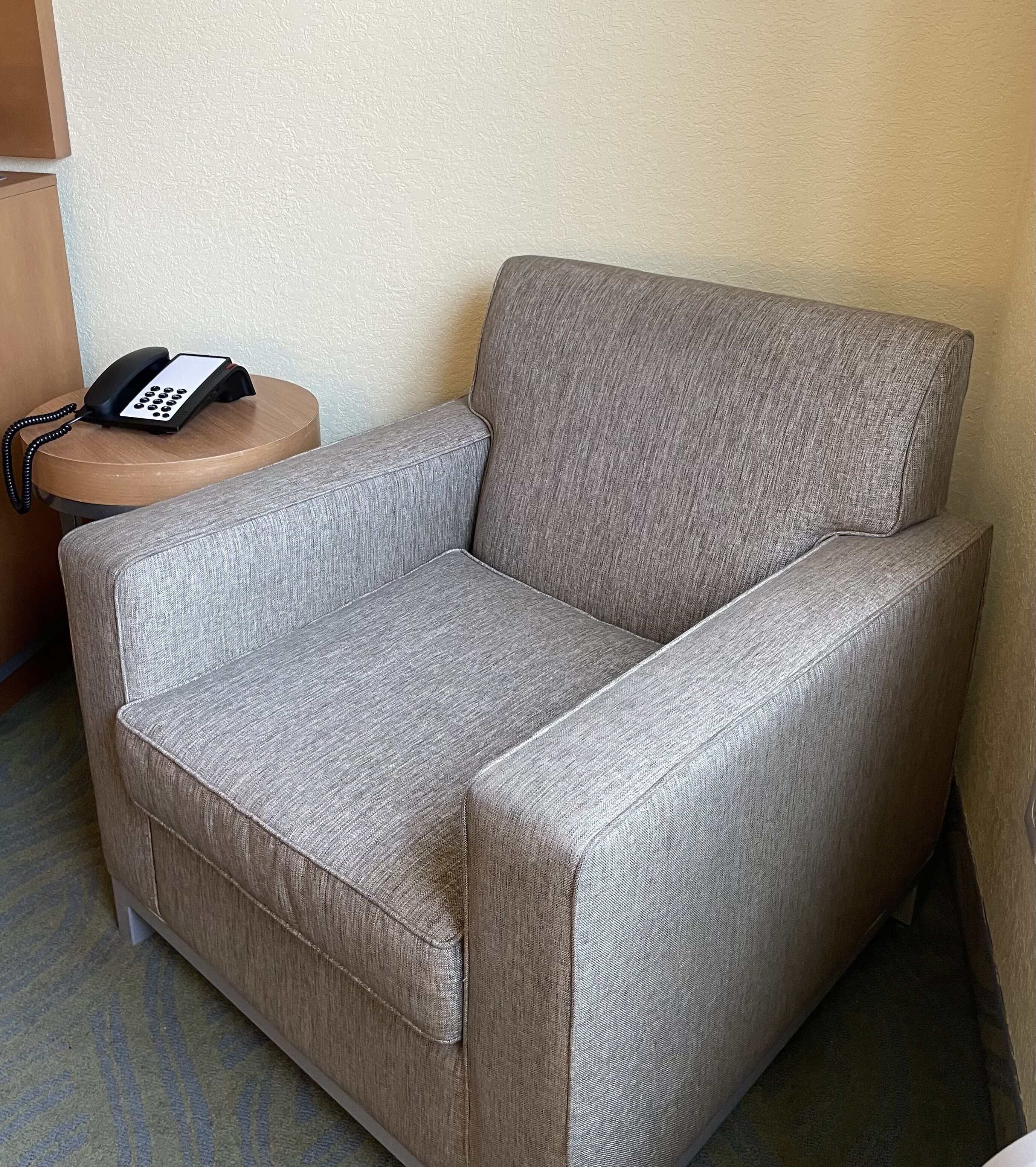 Un sillón gris con un teléfono sobre una mesita de madera.