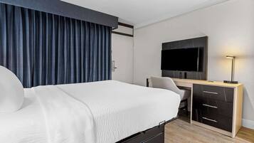 A modern hotel room with a large bed, a desk, a flat-screen TV, and a desk lamp.