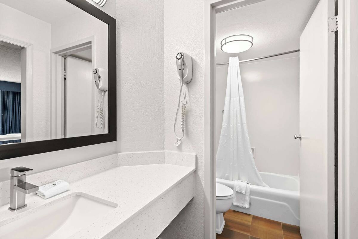 A modern bathroom with a white sink, a large mirror, a hairdryer, a shower curtain, and a bathtub.