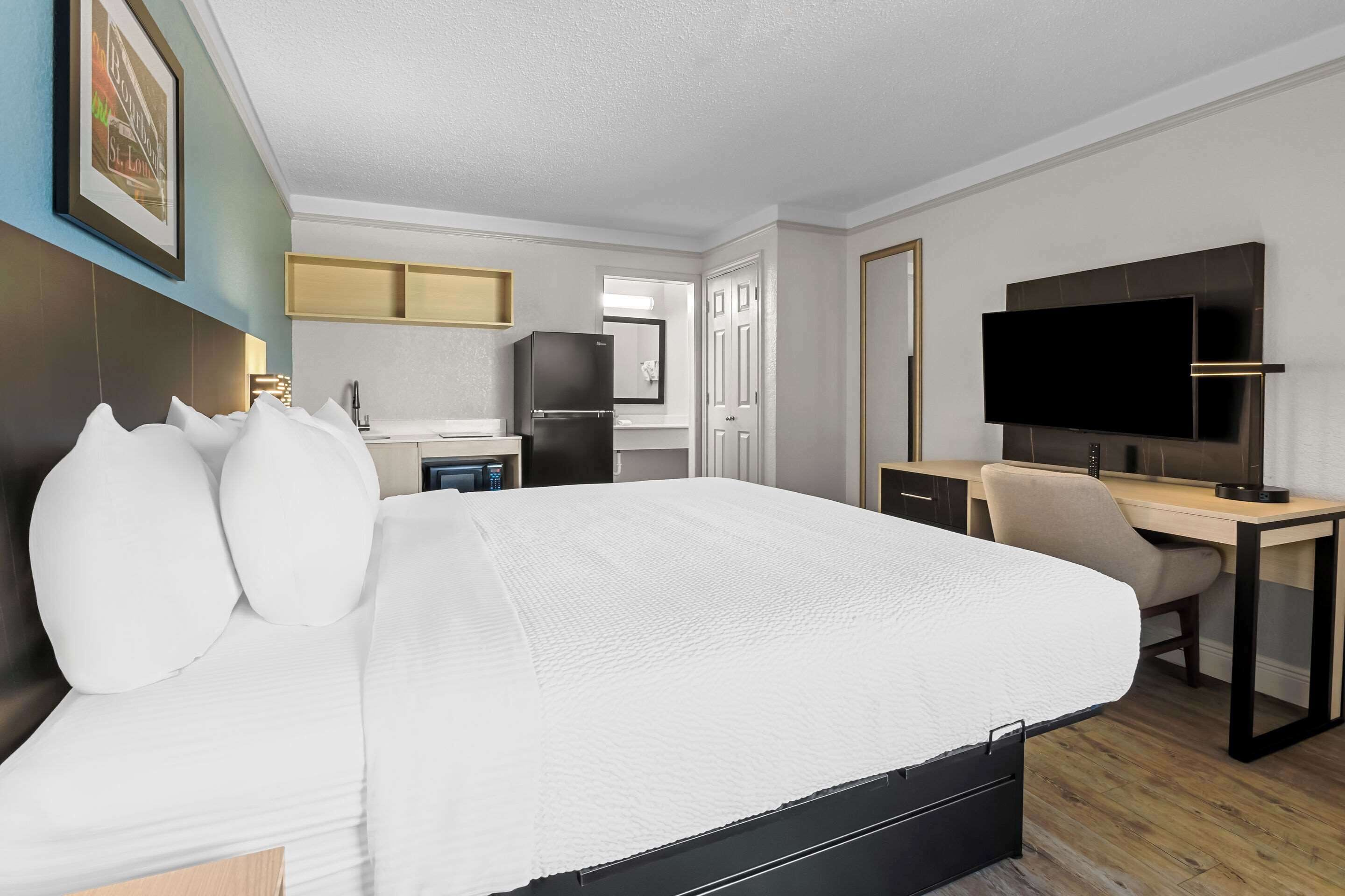 Moderni hotellihuone, jossa on suuri sänky, työpöytä, taulutelevisio ja pieni keittiönurkkaus.