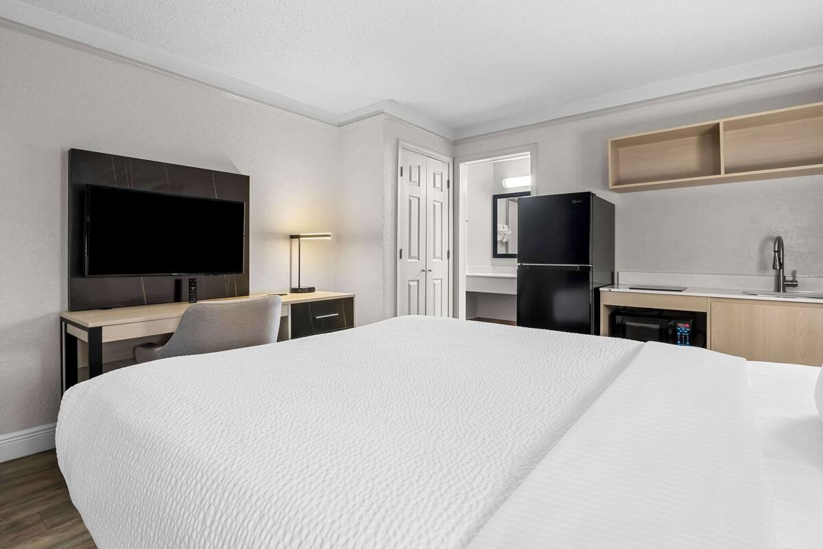A hotel room with a large bed, a desk with a chair, a flat-screen TV, a refrigerator, a microwave, and a sink.