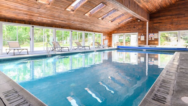 An indoor swimming pool with clear blue water, wooden ceiling, and large windows offering views of greenery. - Quality Inn Bourne - Cape Cod (Buzzards Bay)