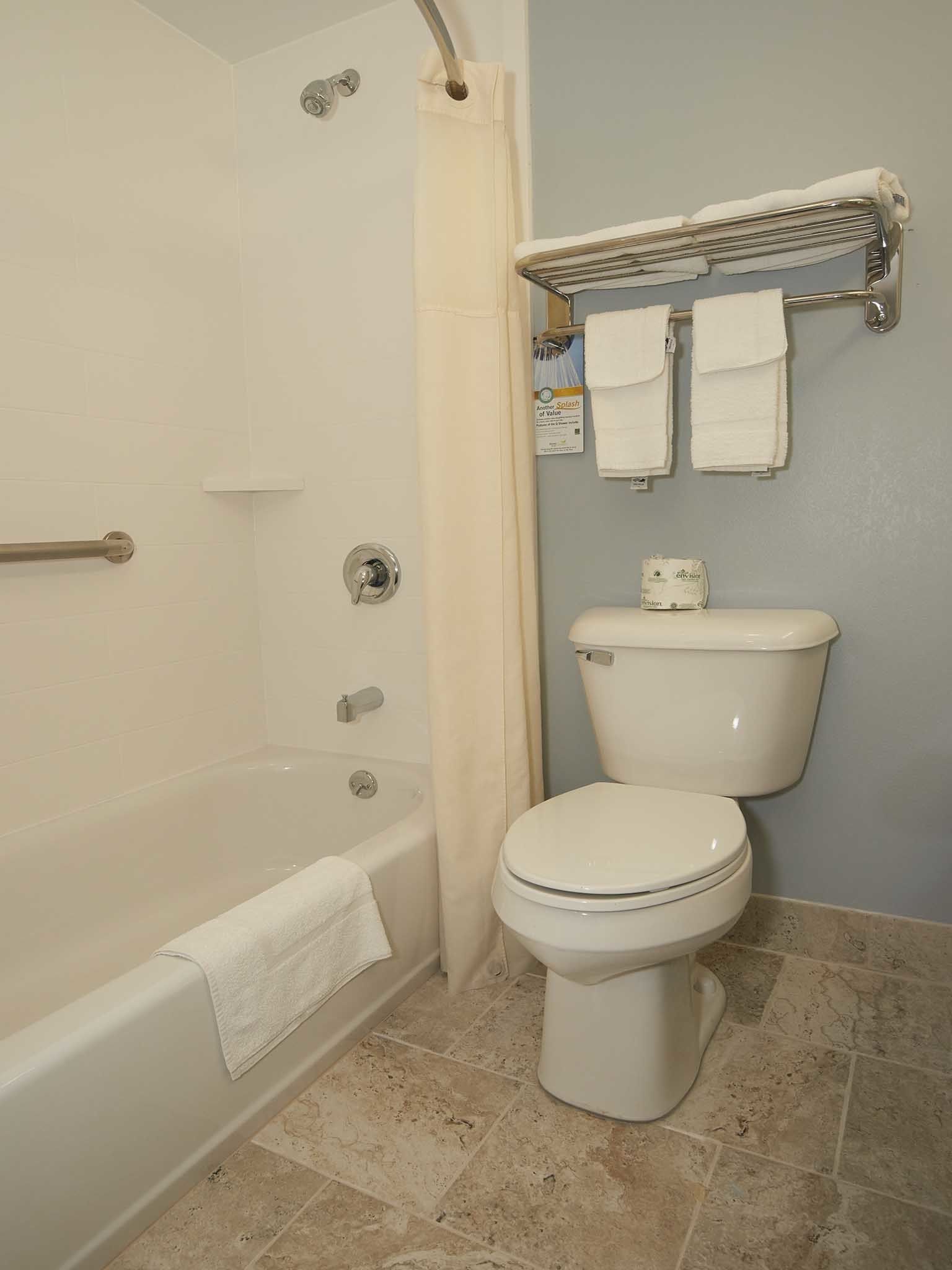 A bathroom with a bathtub, toilet, and a towel rack with two towels.