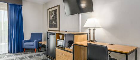 A hotel room with a desk, chair, TV, and a painting on the wall.