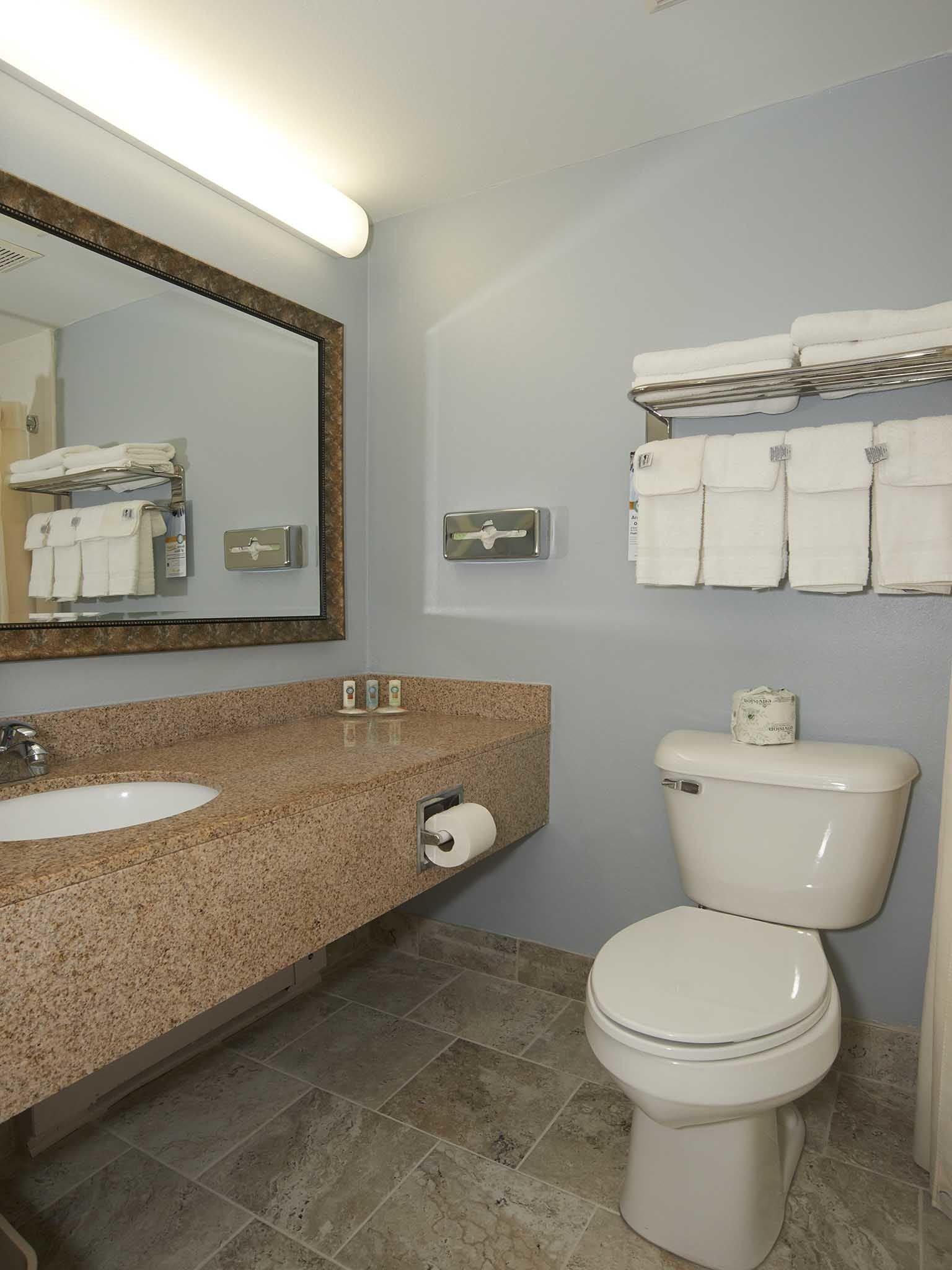 A bathroom with a granite countertop sink, a white toilet, and a towel rack with folded towels.