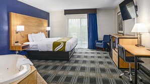 A hotel room with a bed, a desk, a chair, a TV, a bathroom with a bathtub, and a window with curtains. - Quality Inn Bourne - Cape Cod (Buzzards Bay)