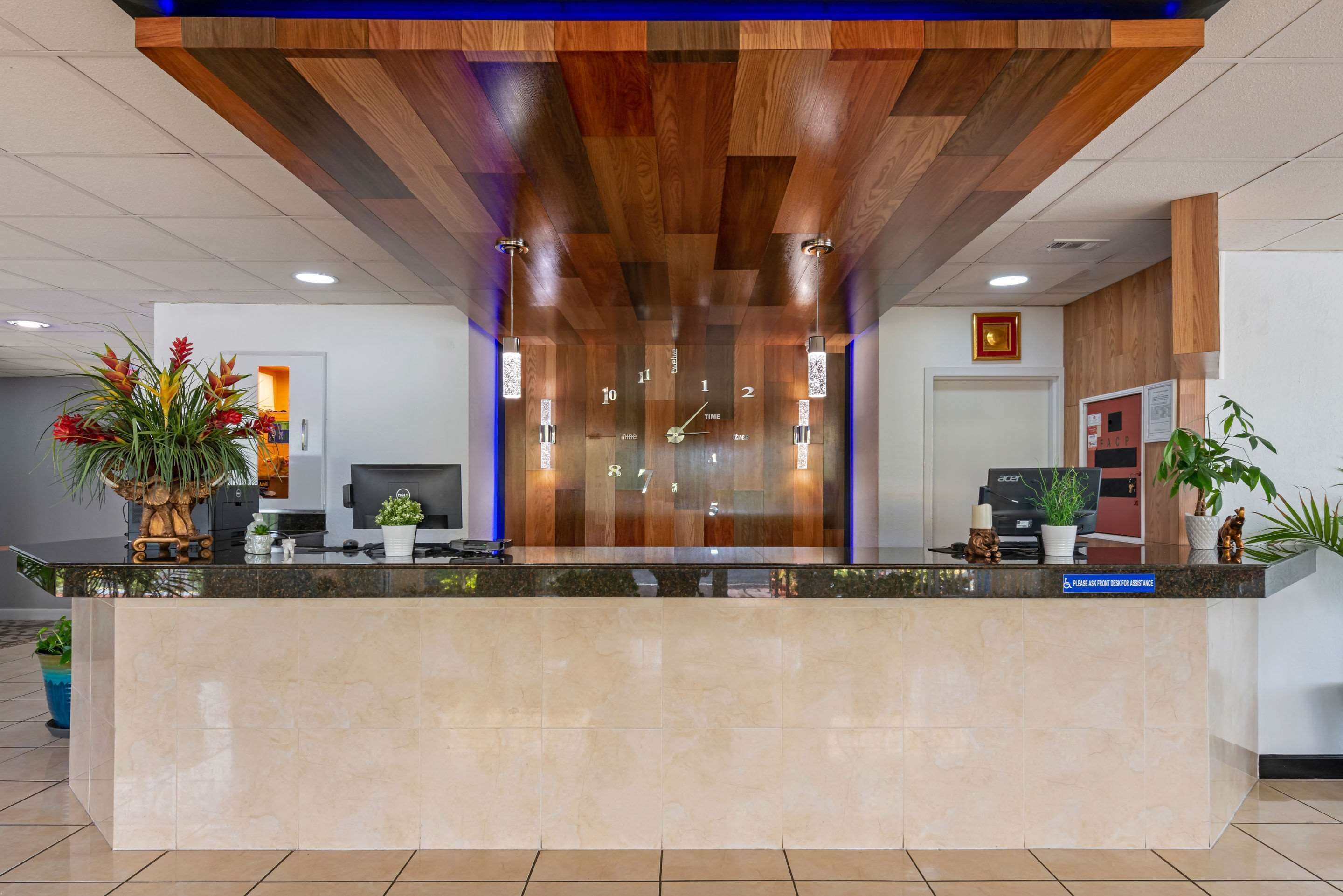 A reception desk with a wooden ceiling, a digital clock, and a sign instructing to use the self-service kiosk.
