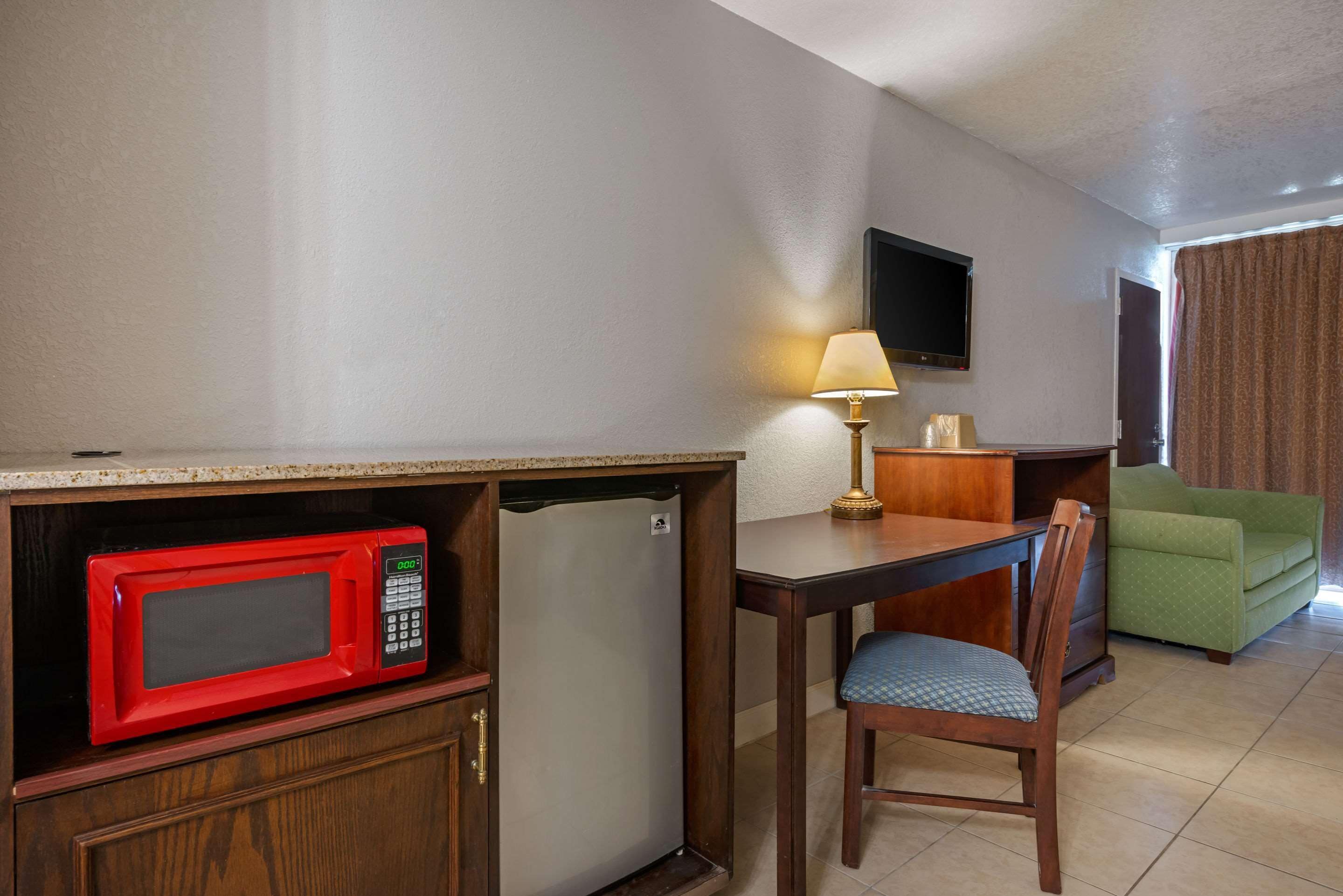 Une chambre d’hôtel compacte comprenant un coin cuisine, un espace repas avec une table et une chaise, un canapé vert et un téléviseur à écran plat fixé au mur.