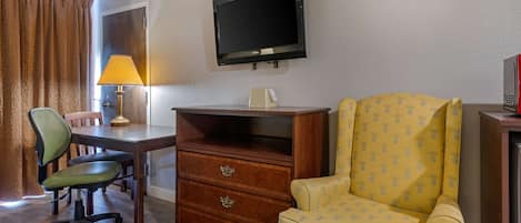 Une chambre d’hôtel avec un bureau en bois, une chaise, un téléviseur fixé au mur et un fauteuil à motifs.
