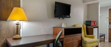 A compact room with a desk, a chair, a television mounted on the wall, and a microwave.