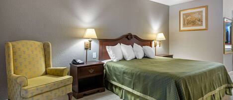 Una habitación de hotel con una cama, dos mesitas de noche, una silla y una lámpara de pared.