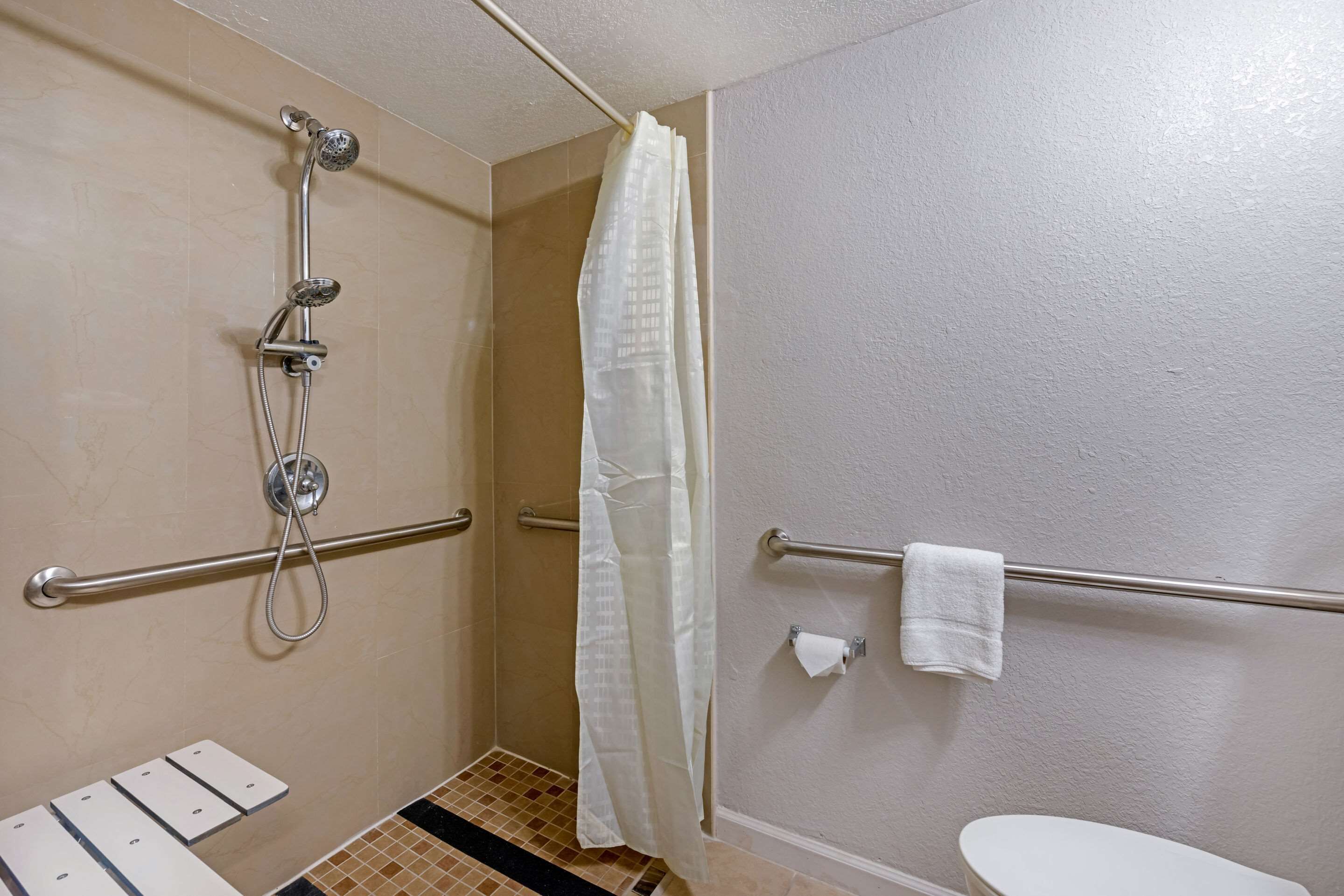 A bathroom with a shower, grab bars, a toilet, and a towel rack.