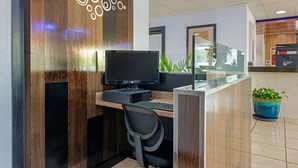 A reception desk with a computer, a chair, and a potted plant. - Rodeway Inn Clermont North (Clermont)