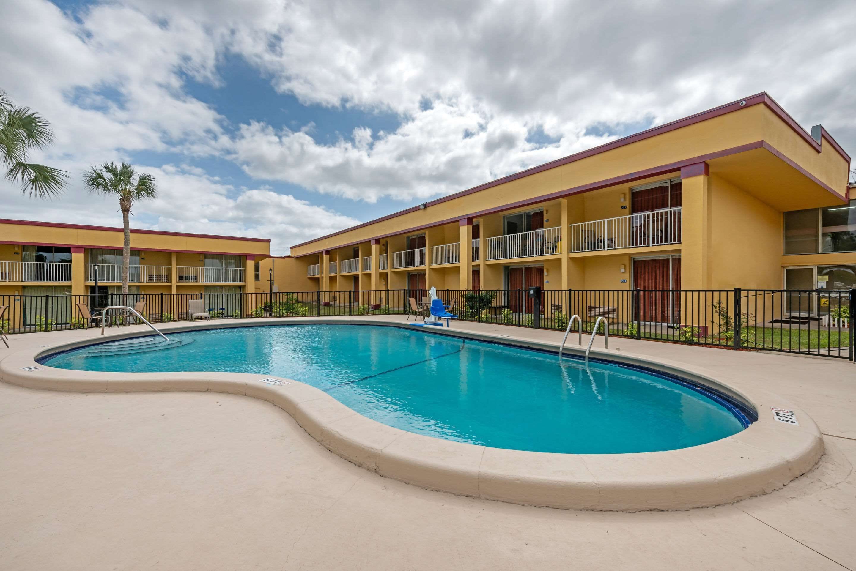 A hotel with a swimming pool, multiple balconies, and a clear sky.