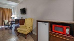 A hotel room with a wooden desk, a yellow armchair, a television mounted on the wall, and a microwave on a wooden cabinet. - Rodeway Inn Clermont North (Clermont)