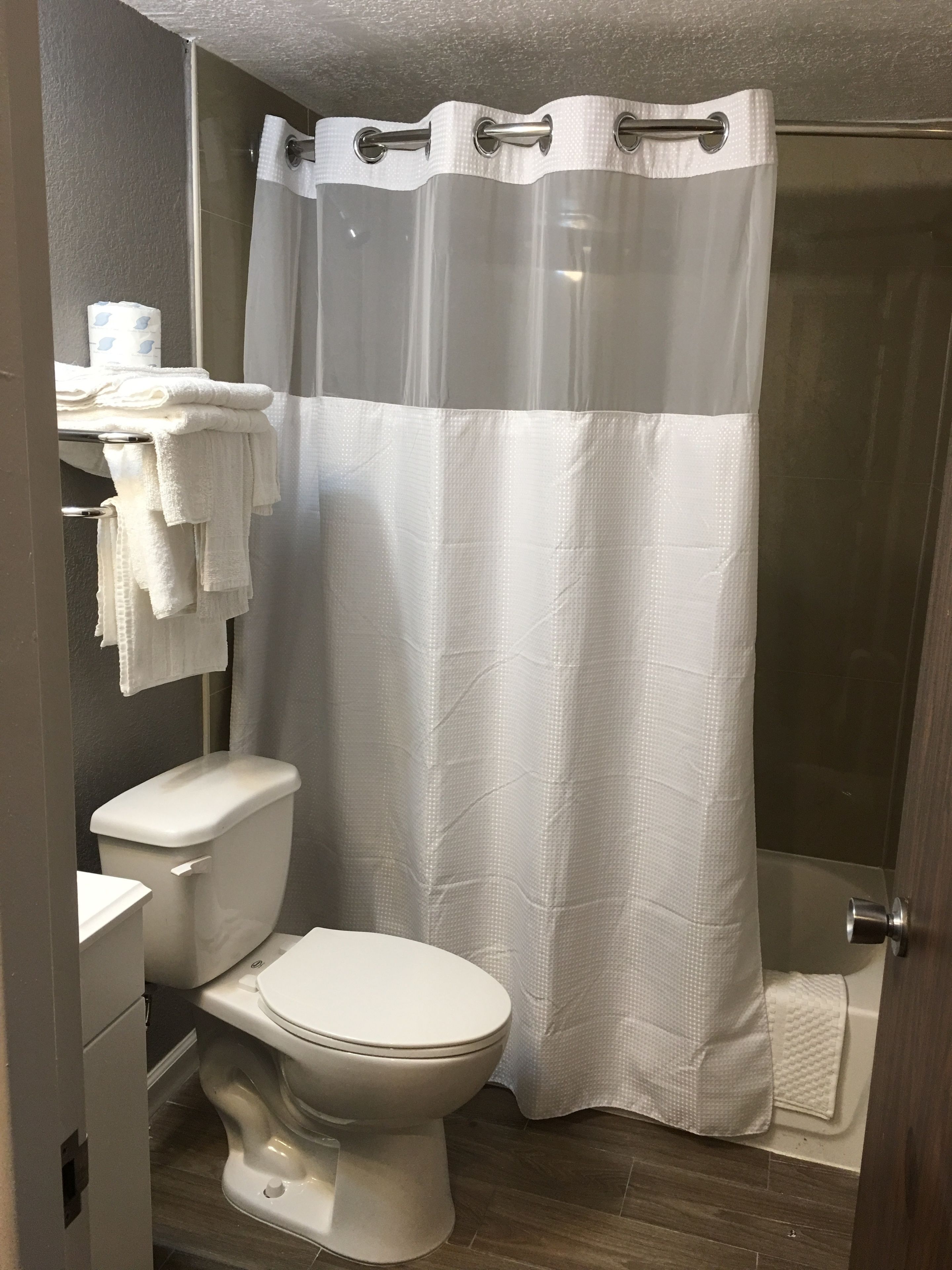 A bathroom with a toilet, a towel rack with folded towels, and a shower curtain.