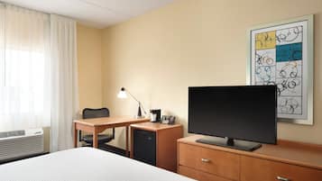 A hotel room with a bed, desk, chair, television, and a framed artwork on the wall.