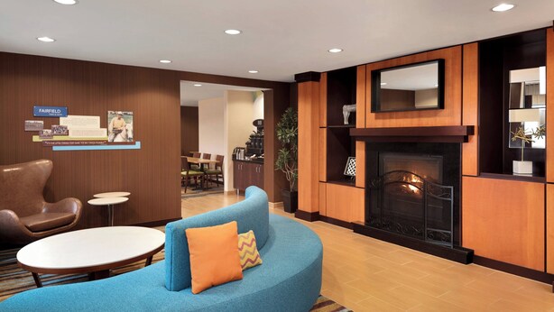 Un vestíbulo de hotel moderno con un sofá azul curvo, una chimenea y un área de comedor visible a través de un vano abierto.