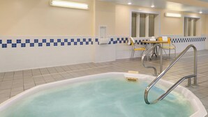 Zona de piscina con jacuzzi, una mesa y sillas, y un ventanal.