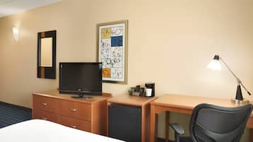 Une chambre d’hôtel équipée d’un lit, d’un bureau avec un ordinateur, d’une lampe de bureau, d’un petit réfrigérateur et d’un téléviseur fixé au mur.