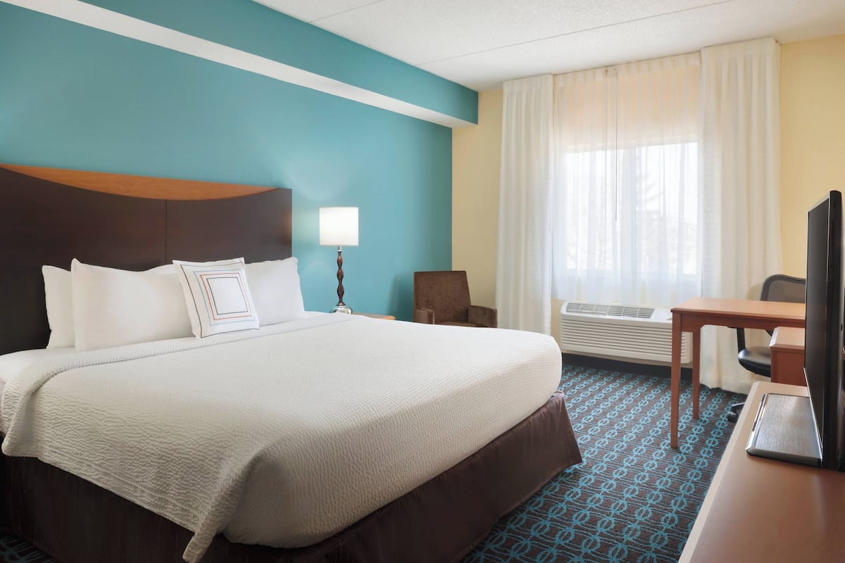 Habitación de hotel con una cama grande, un escritorio, una silla, un televisor y una ventana con cortinas.