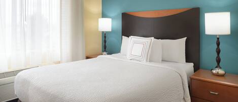 A hotel room with a large bed, two bedside tables with lamps, a window with sheer curtains, and a teal accent wall.