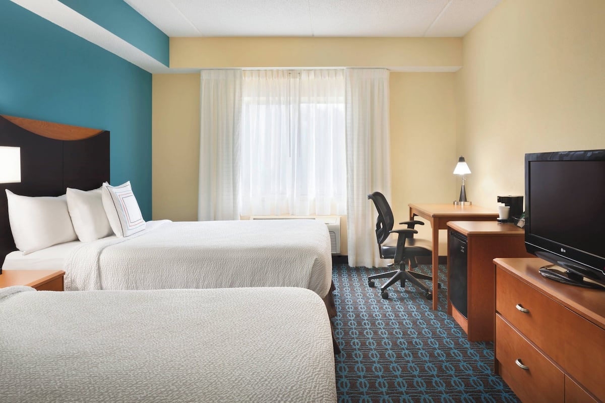 Una habitación de hotel con dos camas, un escritorio con silla, un televisor y una lámpara.