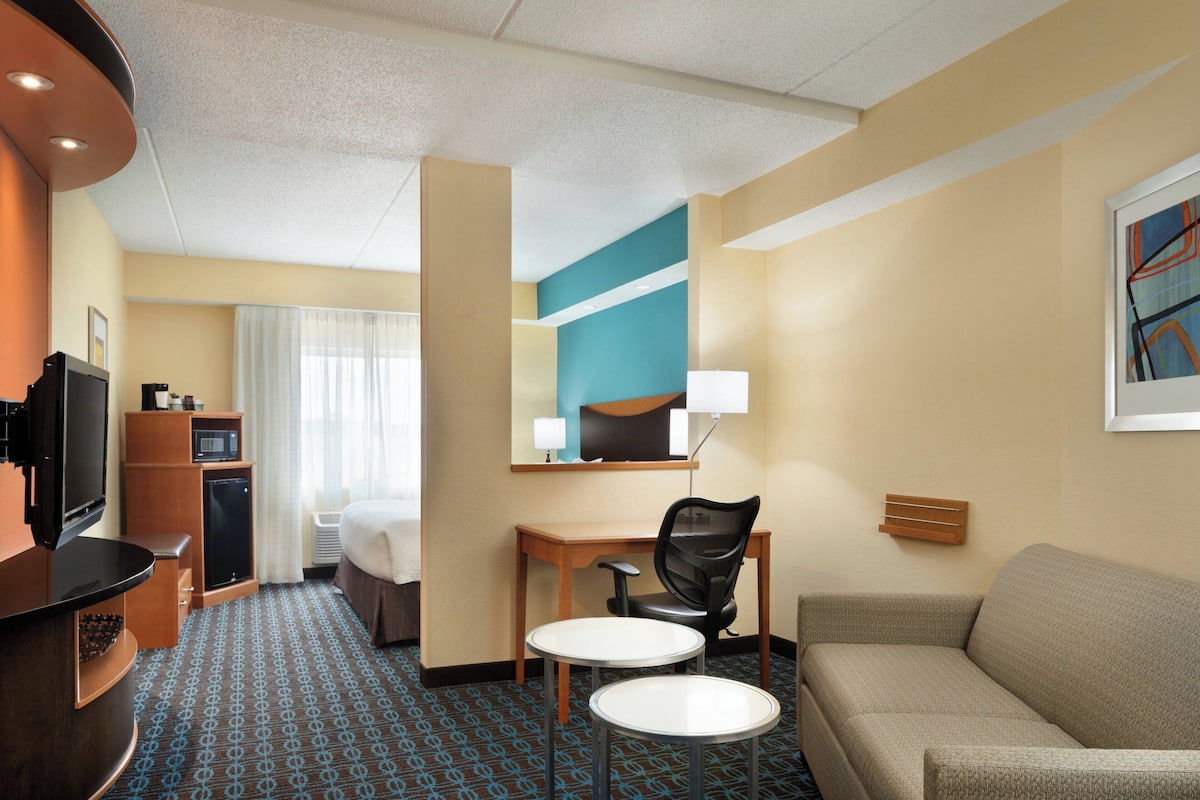 Habitación de hotel con cama, escritorio con silla, televisión, minibar y sofá.