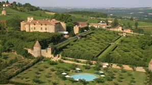 Un castillo con piscina rodeado de jardines cuidados y viñedos.