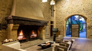 Habitación con paredes de piedra, chimenea, zona de estar y un amplio ventanal de arco.