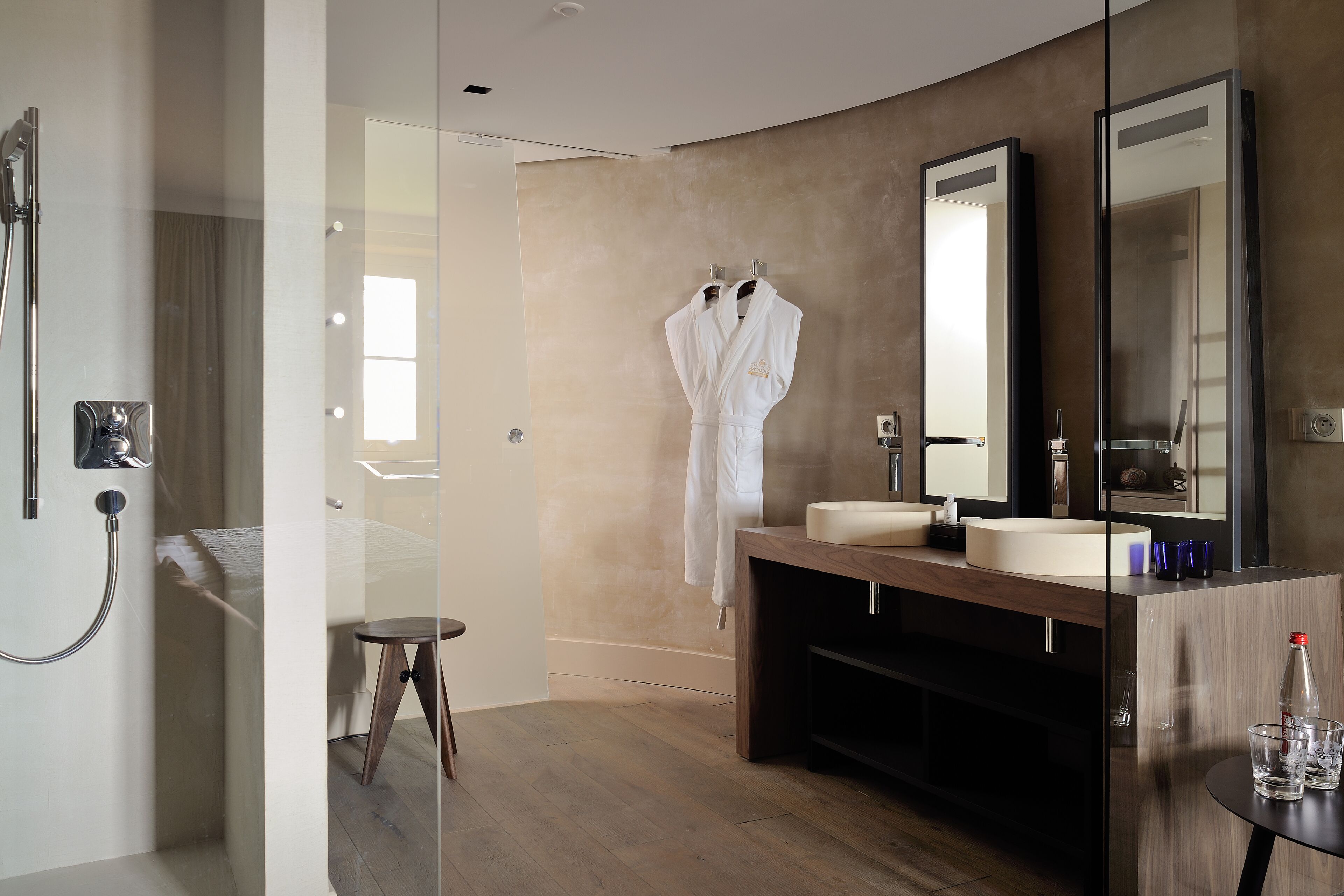 Une salle de bain moderne avec une douche à parois de verre, un meuble-lavabo en bois doté d’un grand miroir et une serviette de bain accrochée au mur.