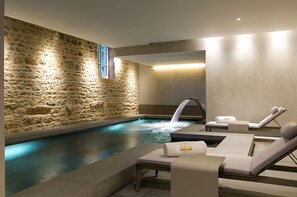 A spa area with a stone wall, a hot tub, and lounge chairs. - Chateau de BAGNOLS (Bagnols)