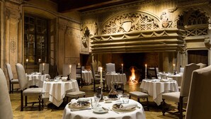 Un comedor con mesas redondas dispuestas para cuatro, cada una con mantel blanco, velas y vajilla elegante.