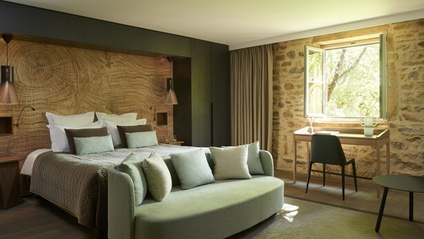 A bedroom with a large bed, a sofa, a desk, and a window with a view of trees. - Chateau de BAGNOLS (Bagnols)