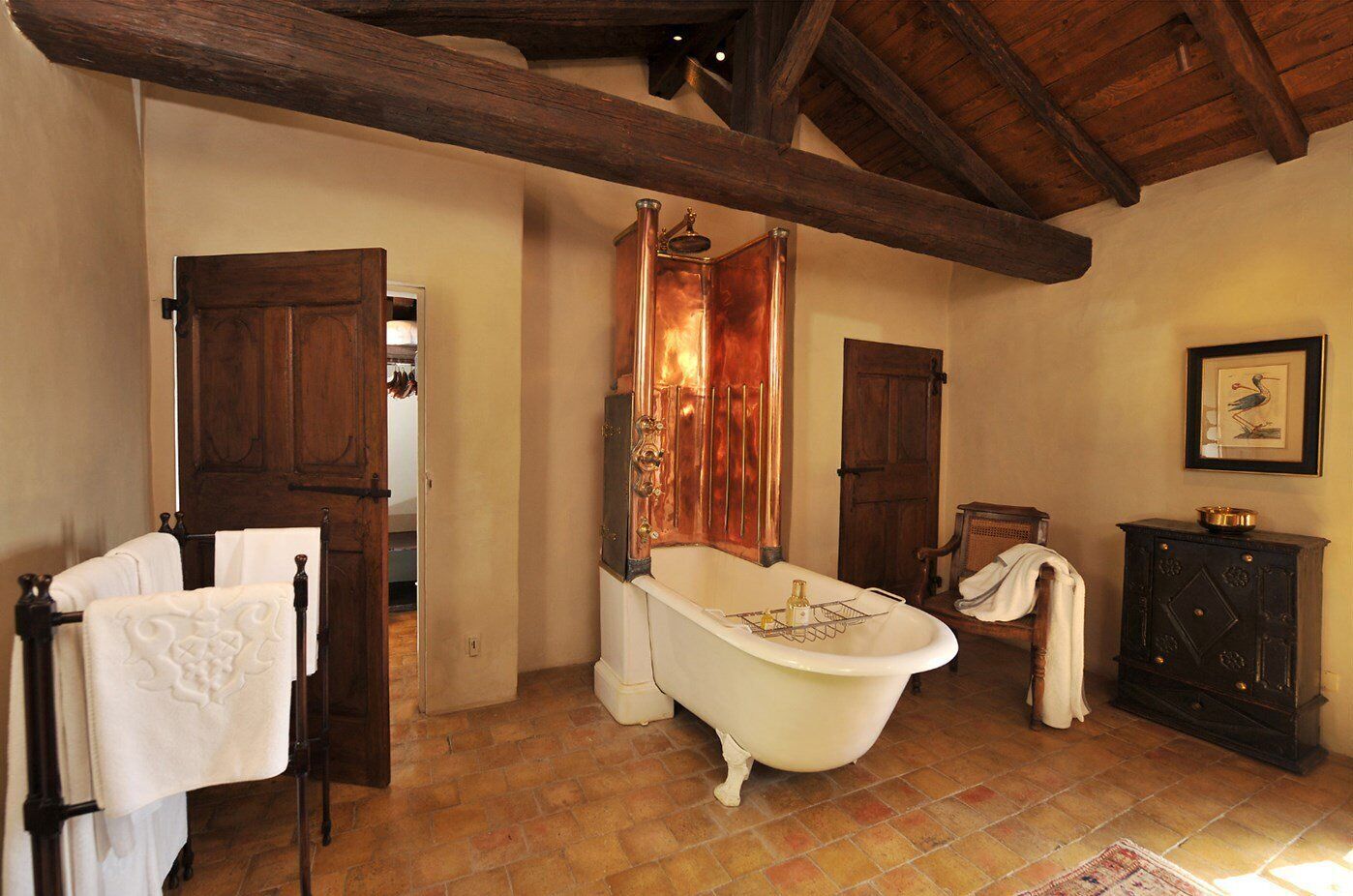 Un baño tradicional con una bañera tipo patas de león, armarios de madera y un techo rústico.