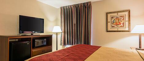 Habitación de hotel con cama, televisor, microondas, refrigerador, lámpara y cortina.