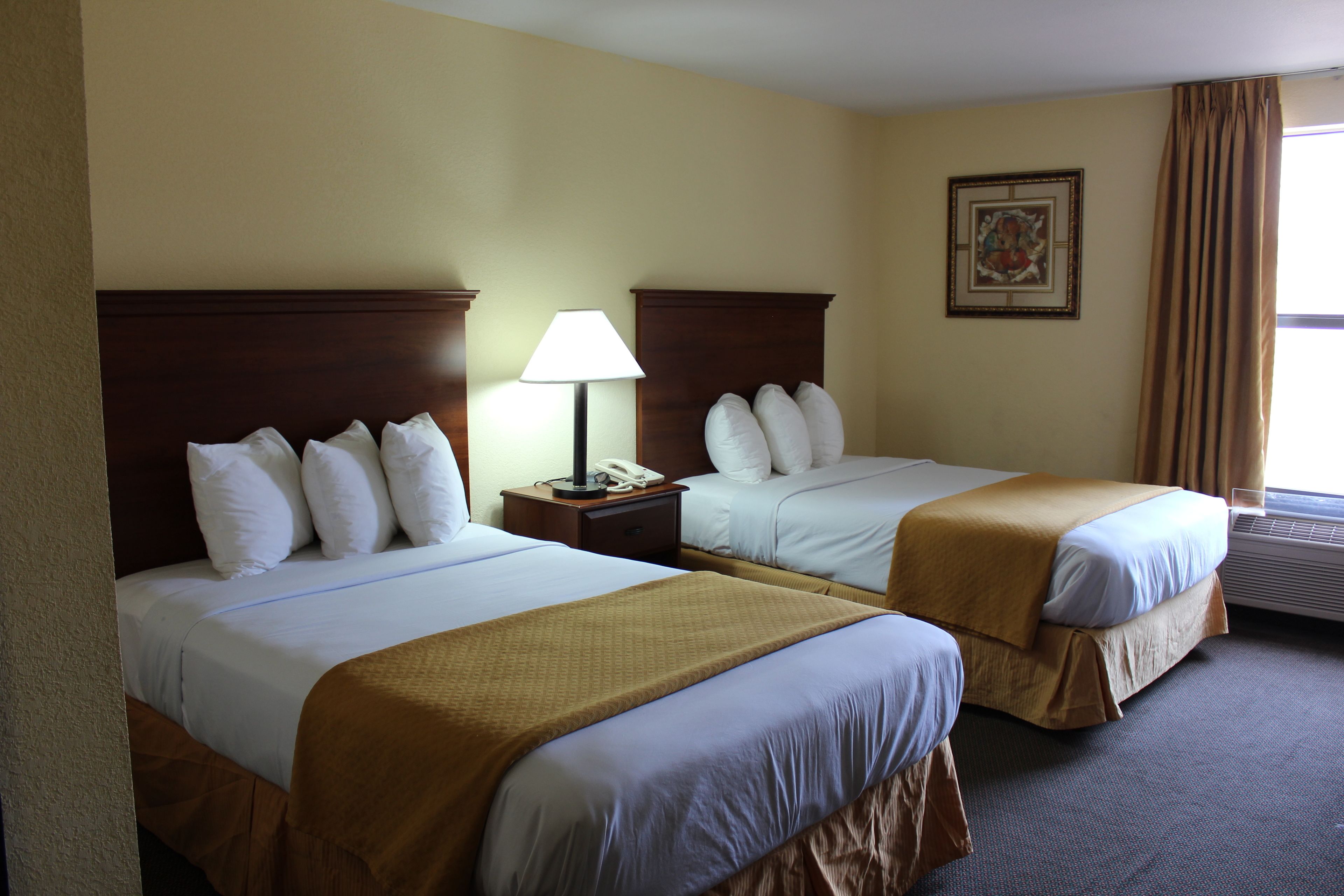 A hotel room with two beds, a nightstand with a lamp, a framed picture on the wall, and a window with curtains.