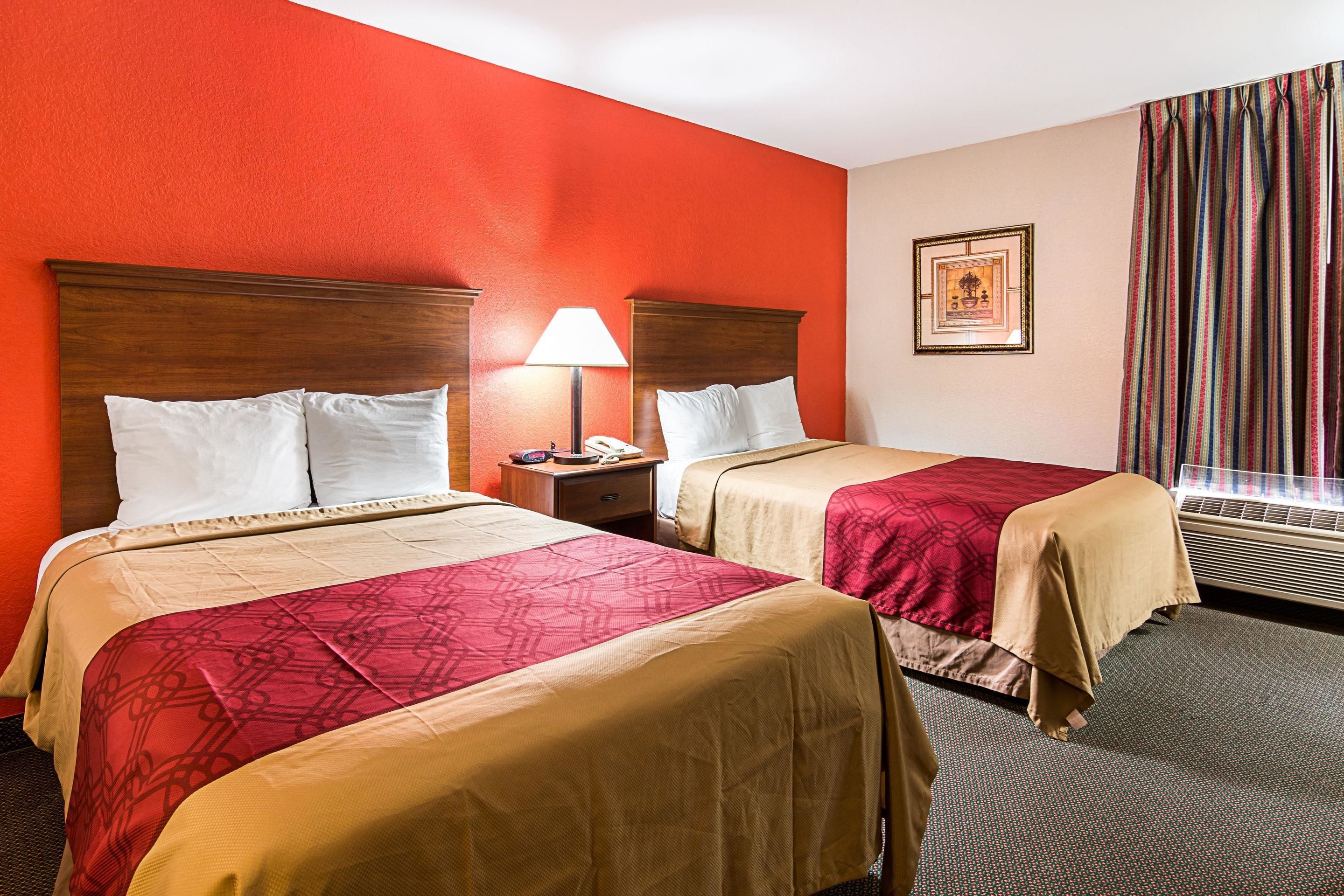 Una habitación de hotel con dos camas, una mesita de noche con una lámpara, un cuadro en la pared y una ventana con cortinas.