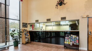 A reception area with a tiled floor, a potted plant, a bulletin board, and a window with a view of the outside. - Econo Lodge Andrews Air Force Base (Clinton)