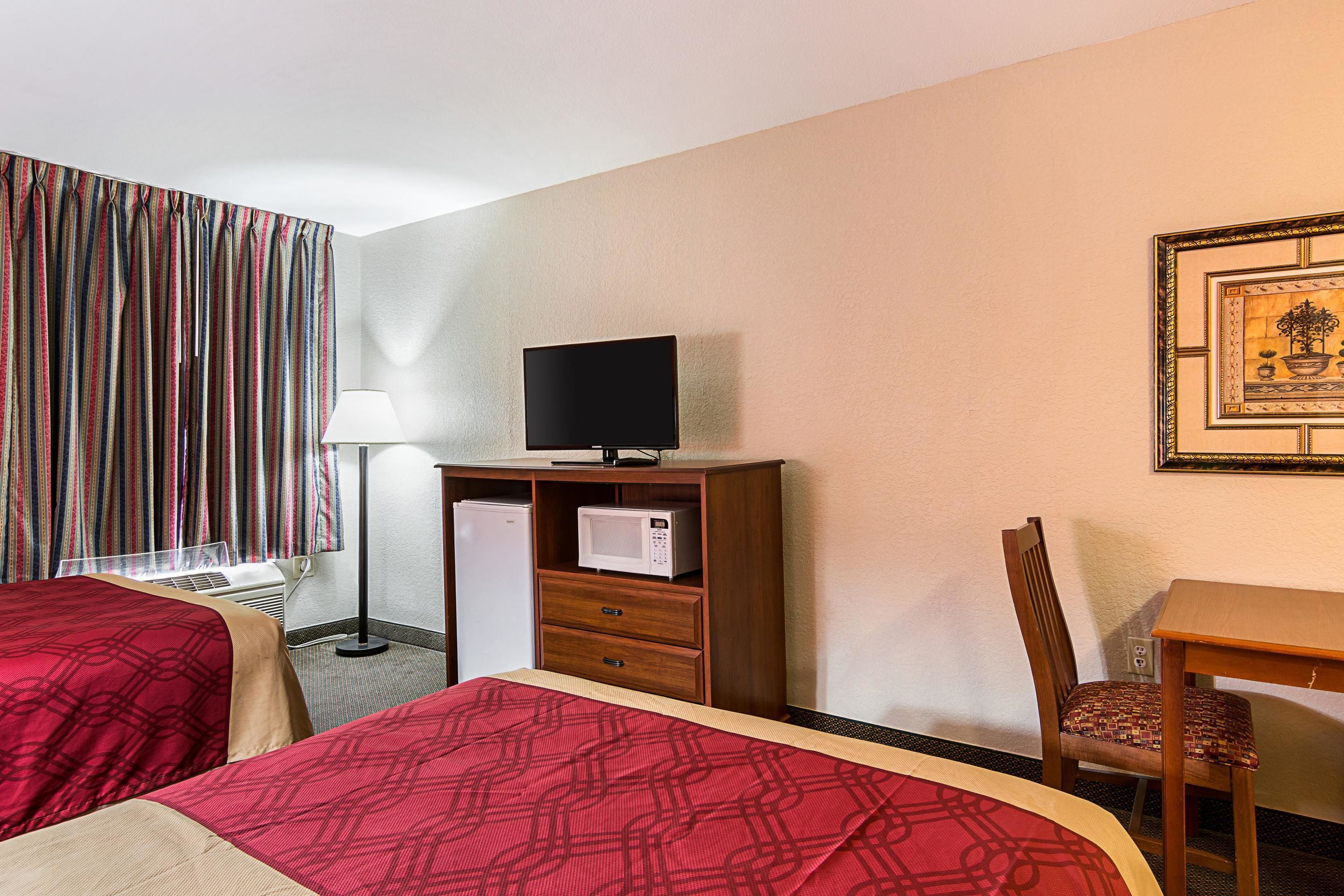 A hotel room with two beds, a desk, a chair, a television, a microwave, and a window with curtains.