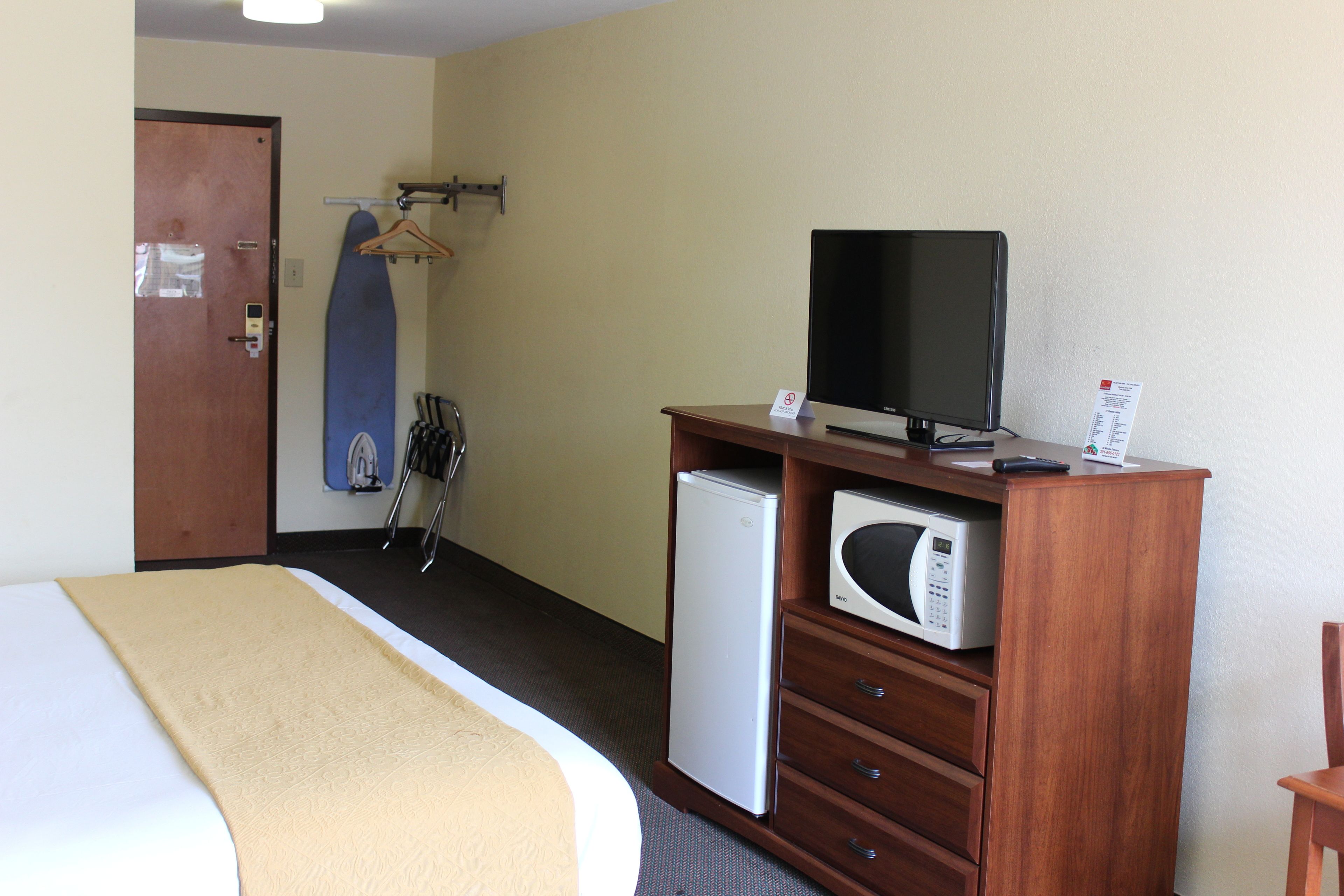 Habitación de hotel con cama, televisión, microondas, refrigerador pequeño y perchero.