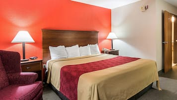 Una habitación de hotel con una cama, dos mesitas de noche, una silla y una puerta.