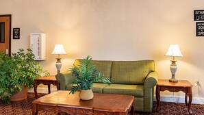 A room with a green sofa, two wooden side tables with lamps, a wooden coffee table, and a potted plant. - Econo Lodge Andrews Air Force Base (Clinton)