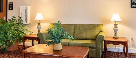 A room with a green sofa, two wooden side tables with lamps, a wooden coffee table, and a potted plant.